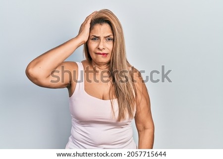 Middle age hispanic woman wearing casual style with sleeveless shirt confuse and wonder about question. uncertain with doubt, thinking with hand on head. pensive concept. 