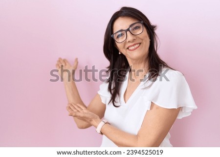 Middle age hispanic woman wearing casual white t shirt and glasses inviting to enter smiling natural with open hand  Foto stock © 