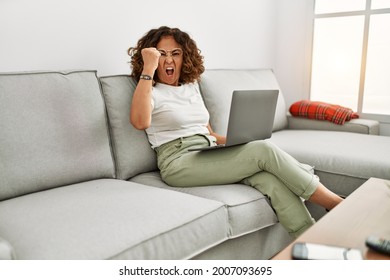 Middle Age Hispanic Woman Working Using Computer Laptop At Home Annoyed And Frustrated Shouting With Anger, Yelling Crazy With Anger And Hand Raised 