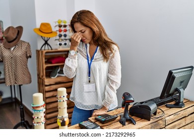 Middle age hispanic woman working as manager at retail boutique tired rubbing nose and eyes feeling fatigue and headache. stress and frustration concept. 