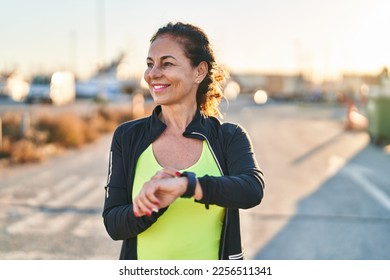 Middle age hispanic woman working out with smart watch outdoors - Powered by Shutterstock