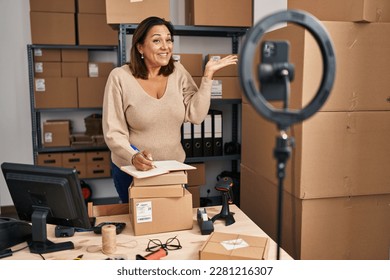 Middle age hispanic woman working at small business ecommerce doing online tutorial celebrating achievement and happy smile   winner expression and raised hand 