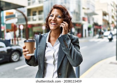 Middle age latin businesswoman drinking coffee and talking on the smartphone at the city. - Powered by Shutterstock