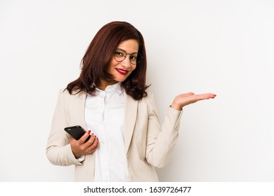 Middle Age Latin Woman Holding A Mobile Phone Isolated Showing A Copy Space On A Palm And Holding Another Hand On Waist.