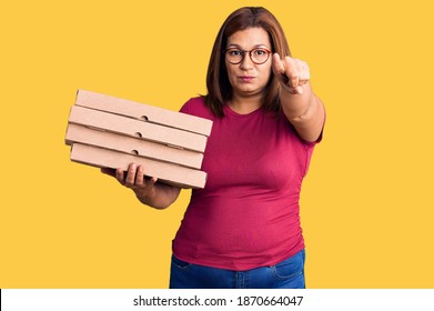 Middle Age Latin Woman Holding Delivery Pizza Box Pointing With Finger To The Camera And To You, Confident Gesture Looking Serious 