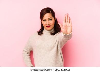 Middle age latin woman isolated on a pink background standing with outstretched hand showing stop sign, preventing you.