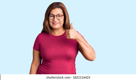Middle age latin woman wearing casual clothes and glasses smiling happy and positive, thumb up doing excellent and approval sign 