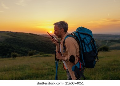 Middle Age Male Hiker With Backpacker Communicating With A Walkie Talkie During Sunset