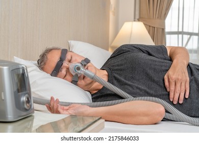 Middle age male with sleep apnea wearing CPAP headgear and mask while sleeping in his bedroom - Shutterstock ID 2175846033