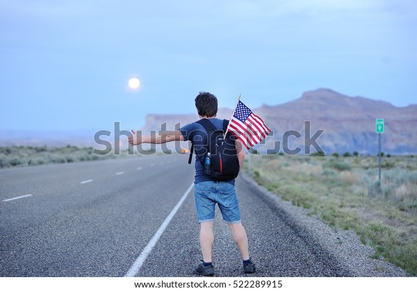 Middle age male tourist with american flag\
in backpack hitchhiking along a desolate\
road