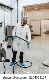 Middle Age Male Working In Industrial Slaughterhouse And Finishing His Daily Job. He Is Cleaning And Washing Food Processing Plant Floor And Machinery Production Lines With Water.