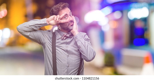 Middle Age Man, With Beard And Bow Tie Looking At Camera Through Fingers In Victory Gesture Winking The Eye And Blowing A Kiss At Night Club