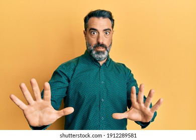 Middle age man with beard and grey hair wearing business clothes afraid and terrified with fear expression stop gesture with hands, shouting in shock. panic concept. 