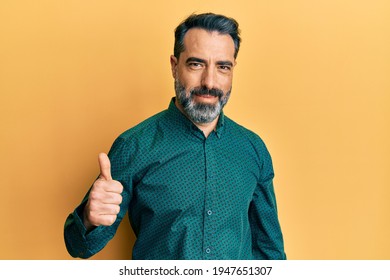 Middle age man with beard and grey hair wearing business clothes doing happy thumbs up gesture with hand. approving expression looking at the camera showing success. 