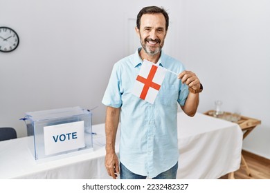 Middle age man with beard at political campaign election holding england flag looking positive and happy standing and smiling with a confident smile showing teeth  - Shutterstock ID 2232482327