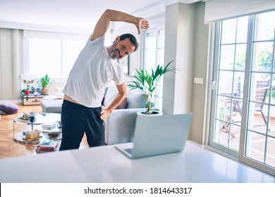 Middle Age Man With Beard Training And Stretching Doing Exercise At Home Looking At Sport Video On Computer