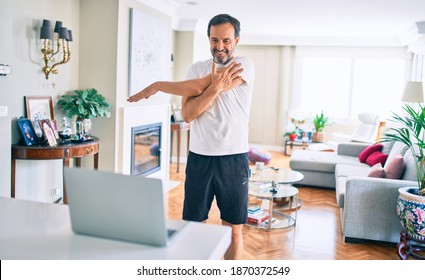 Middle Age Man With Beard Training And Stretching Doing Exercise At Home Looking At Sport Video On Computer