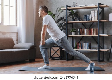 Middle age man doing fitness workouts at home. Get fit at home. Full length shot of active man training on laptop, exercising, stretching during morning workout at home. Sport, healthy lifestyle. - Powered by Shutterstock