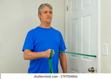 Middle Age Man Doing Shoulder Surgery Physical Therapy With Resistance Rubber Band Exercises At Home To Strengthen The Deltoid Muscles To Fully Recover Normal Strength And Flexibility.