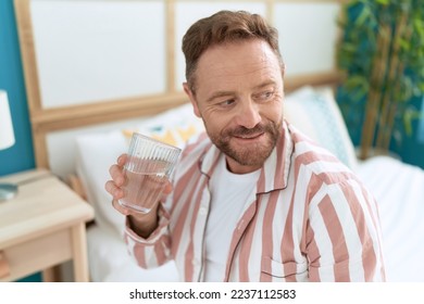 Middle age man drinking glass of water sitting on bed at bedroom - Powered by Shutterstock