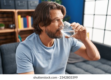 Middle age man drinking glass of water sitting on sofa at home - Powered by Shutterstock