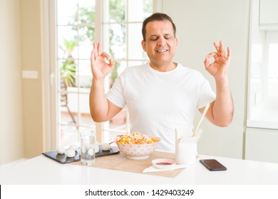 Middle Age Man Eating Asian Food With Chopsticks At Home Relax And Smiling With Eyes Closed Doing Meditation Gesture With Fingers. Yoga Concept.