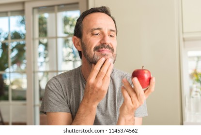 Middle Age Man Eating Healthy Red Apple Serious Face Thinking About Question, Very Confused Idea