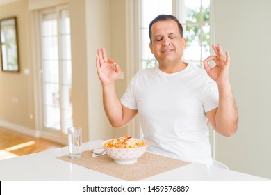 Middle Age Man Eating Rice At Home Relax And Smiling With Eyes Closed Doing Meditation Gesture With Fingers. Yoga Concept.