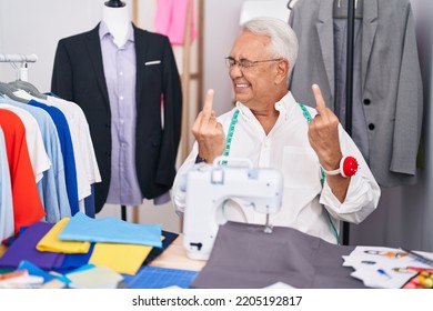 Middle Age Man With Grey Hair Dressmaker Using Sewing Machine Showing Middle Finger Doing Fuck You Bad Expression, Provocation And Rude Attitude. Screaming Excited 