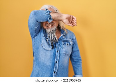 Middle Age Man With Grey Hair Standing Over Yellow Background Covering Eyes With Arm Smiling Cheerful And Funny. Blind Concept. 