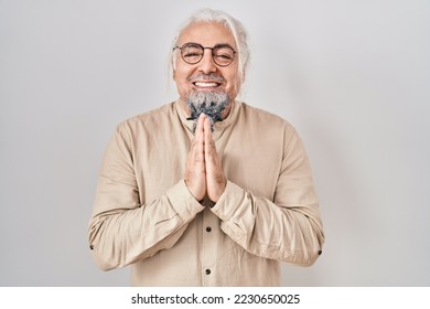 Middle age man with grey hair standing over isolated background praying with hands together asking for forgiveness smiling confident.  - Shutterstock ID 2230650025