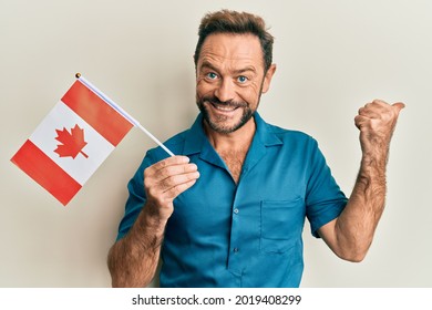 Middle Age Man Holding Canada Flag Pointing Thumb Up To The Side Smiling Happy With Open Mouth 