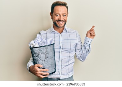 Middle Age Man Holding Paper Bin Full Of Crumpled Papers Smiling Happy Pointing With Hand And Finger To The Side 