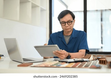 Middle age man interior designer sitting in front of laptop and using digital tablet at workplace - Powered by Shutterstock