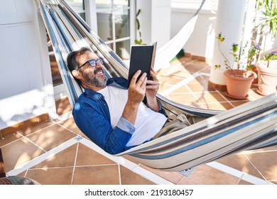 Middle age man reading book lying on hammock at terrace home - Powered by Shutterstock