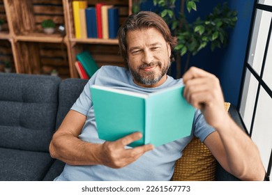 Middle age man reading book sitting on sofa at home - Powered by Shutterstock