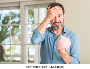 Middle Age Man Save Money On Piggy Bank Stressed With Hand On Head, Shocked With Shame And Surprise Face, Angry And Frustrated. Fear And Upset For Mistake.