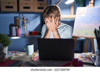 Middle Age Man Sitting At Art Studio With Laptop At Night With Sad Expression Covering Face With Hands While Crying. Depression Concept. 