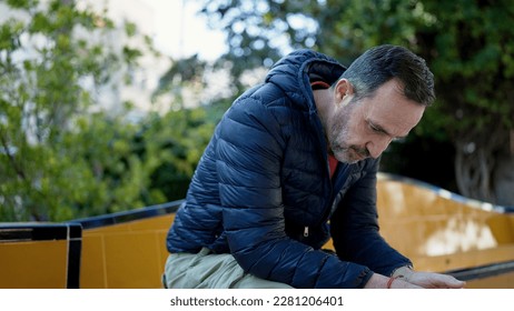 Middle age man sitting on bench with worried expression at park - Powered by Shutterstock