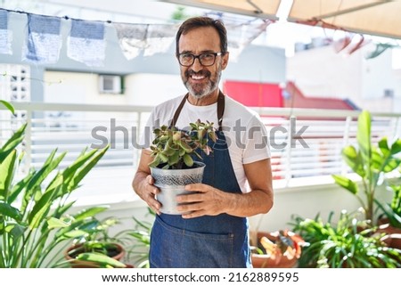 Middle age man smiling confident holding plat pot at terrace home