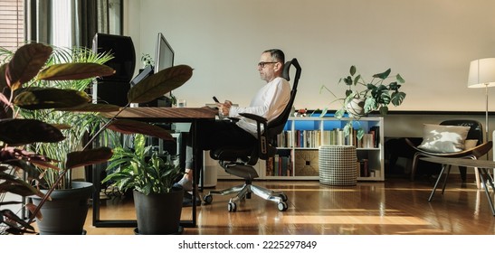 Middle age man smiling while working from home and using phone. - Powered by Shutterstock