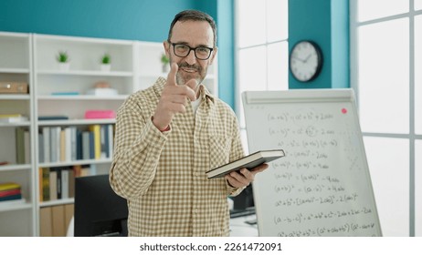 Middle age man teacher teaching lesson holding book at classroom - Powered by Shutterstock