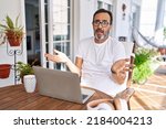 Middle age man using computer laptop at home clueless and confused with open arms, no idea concept. 