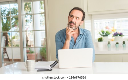 Mann mittleren Alters mit Laptop zu Hause ernstes Gesicht denken über Frage, sehr verwirrte Idee