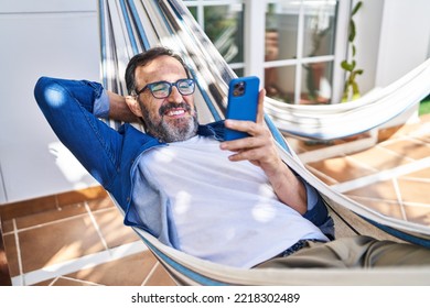 Middle age man using smartphone lying on hammock at terrace home - Powered by Shutterstock