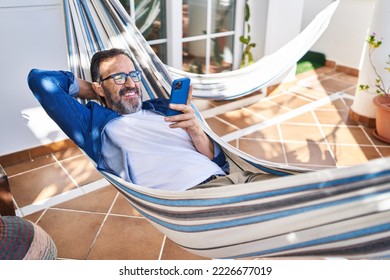 Middle age man using smartphone lying on hammock at terrace home - Powered by Shutterstock