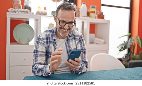 Middle age man using smartphone sitting on table at dinning room - Powered by Shutterstock