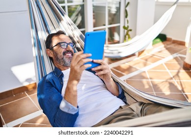 Middle age man using touchpad lying on hammock at terrace home - Powered by Shutterstock