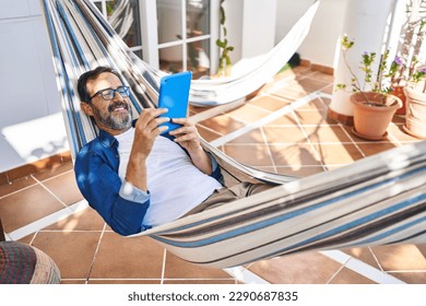 Middle age man using touchpad lying on hammock at terrace home - Powered by Shutterstock