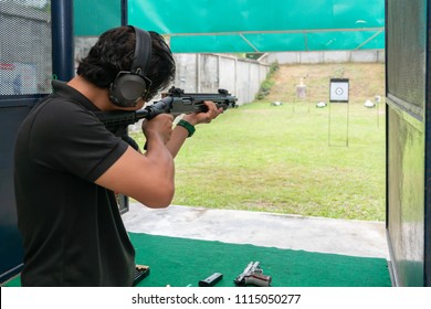 Middle Age Man Wear Ear Plug Standing And Aiming Shotgun At Target In Shooting Range. Men Practicing Fire Pistol Shooting.